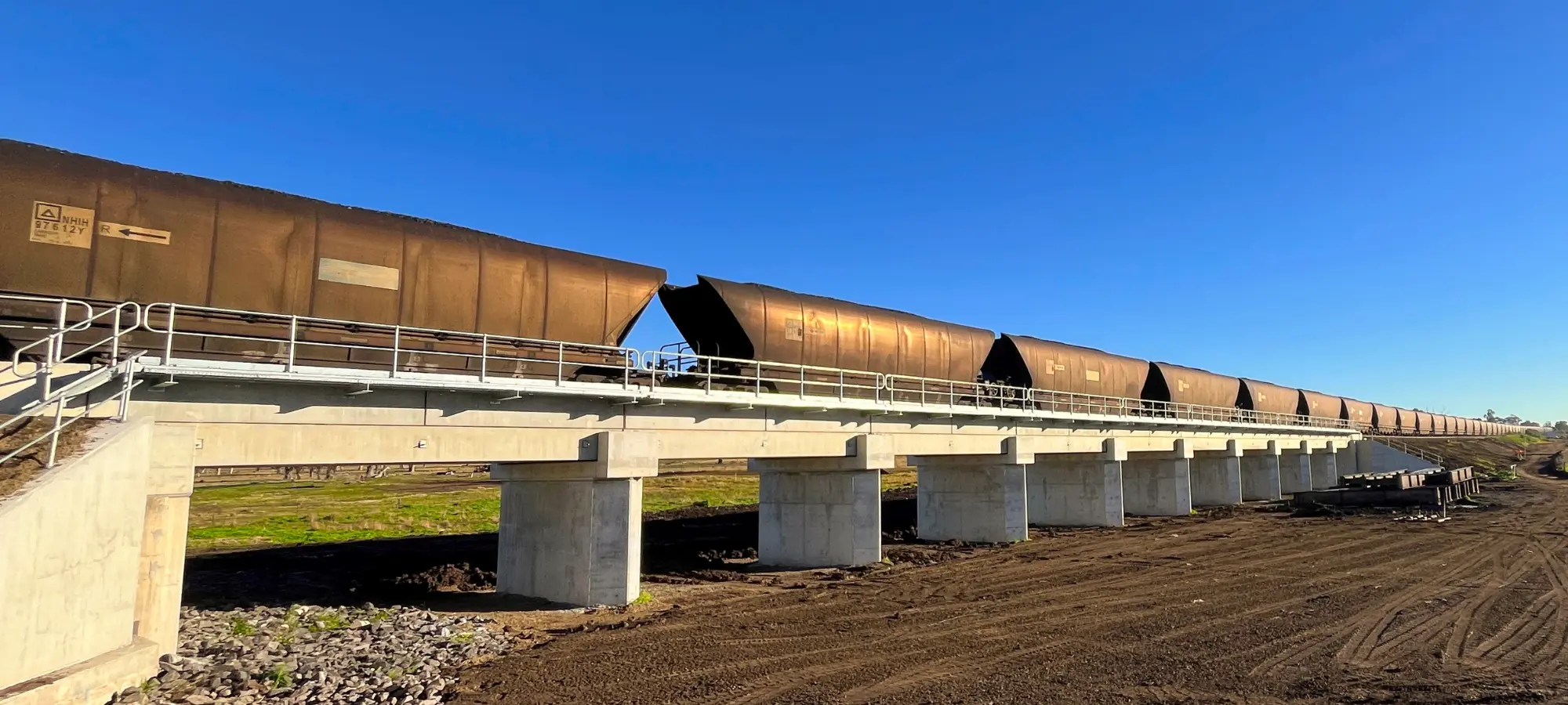 Coal train crossing a new concrete rail viaduct on a row of piers, with freshly graded ground alongside