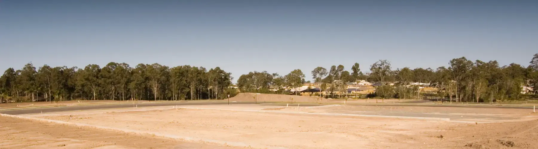 Cleared and graded subdivision land, with a line of gum trees and new houses beyond
