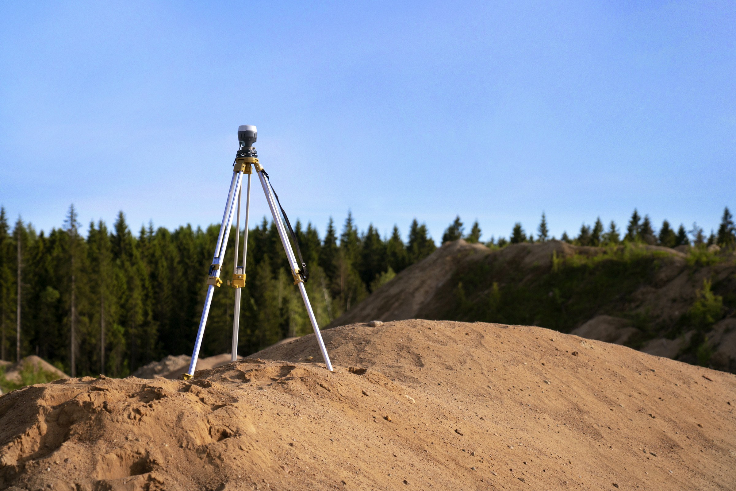 GNSS survey receiver on a tripod set up on an earthworks stockpile